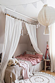 Bed with curtain and round carpet rug in the girls' room in muted colours