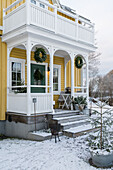 Gelbes Holzhaus mit Balkon und Veranda in verschneitem Garten