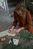 Frau beim Zeichnen, schwarze Farbe und Herbstblätter auf Betonuntergrund