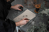 Woman drawing with black paint on card on concrete surface