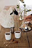Teetassen mit Filz-Manschetten, Designer-Teekanne und Schaf-Figur auf Holztisch
