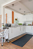 White fitted cabinets in an L-shape and a cart in open plan kitchen