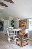 Dining table with children's high chair in open-plan kitchen with white-painted wooden ceiling