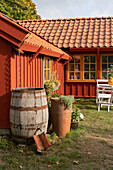 Holzfass vor rot-braunem Holzhaus mit Sprossenfenstern
