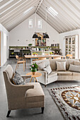 Pale upholstered suite, dining area and kitchen in open-plan interior with gable roof