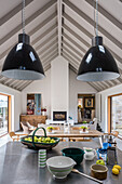 Utensils on kitchen island below pendant lights in open-plan interior with gable roof
