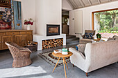 Pale sofa, side table and rattan armchair in front of fireplace