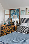 Bett mit blau-weißer Tagesdecke, daneben handbemalte Kommode und Wandspiegel