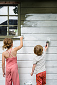 Girl and boy painting outside wall of house