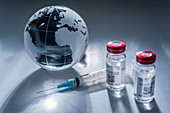 Glass globe and vaccine syringe on gray surface