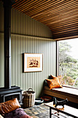 Seating area on window seat and wood-burning stove in room with green wood panelling