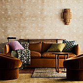 Brown leather couch with cushions, console and wall lamp behind, armchair in foreground