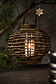 White pillar candle in wooden candle lantern hung from pine branch