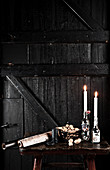 Kerzen in alten Flaschen, Nüsse und Papierrollen auf Tisch vor schwarzer Holztür