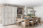 Spacious kitchen-dining room with rattan chairs around dining table and antique cupboard