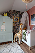 Grey wardrobe, crib with canopy and giraffe figure in the room