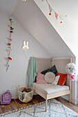 Gemütlicher Stuhl mit Kissen und Blumengirlande im Kinderzimmer im Dachgeschoss