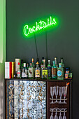 Green neon sign that says cocktails hanging above a bar