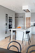 Grey built-in cupboards and central unit with bar stools in an open kitchen