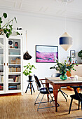 Dining table with bouquet of flowers, vintage chairs and bookcase in living room