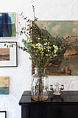 Glass vase with eucalyptus branches in front of picture wall in vintage style