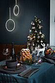 Decorated Christmas table, in the background Christmas tree in front of a dark wall