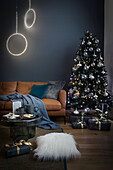 Leather sofa, light objects and a Christmas tree in the living room with a blue wall