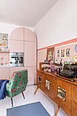 Retro Sideboard, Sessel mit buntem Bezug und Einbauküche mit rosa Fronten