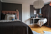 Double bed and table with chair in bedroom with dark grey walls