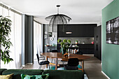 Offener Wohnraum mit schwarzer Einbauküche, Essbereich und grünem Sofa