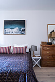 Doppelbett mit Tagesdecke, darüber Bild an weißer Wand