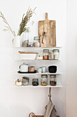 Storage jars, wooden boards and dried grasses on kitchen shelves