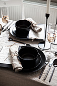 Gedeckter Tisch mit Leinentischdecke und schwarzem Geschirr