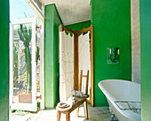 Free-standing bathtub and screen in bathroom with green walls and access to terrace