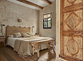 View into the bedroom with double bed, wooden bench and neutral colored walls