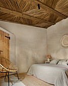 Double bed in bedroom with sand colored walls and thatch reed ceiling