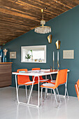 Orangefarbener Essbereich vor blaugrauer Wand in offenem Wohnraum mit rustikaler Holzdecke