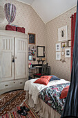 Bed, writing corner and old wardrobe in a children's room with wallpaper