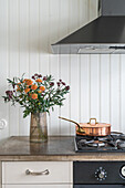 Bouquet of flowers next to gas cooktop with a copper sauce pan