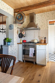 Gas cooker with extractor hood in country-house kitchen with floral wallpaper