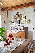 View over dining table to chest of drawers below gallery of pictures in rustic room
