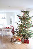 A Christmas tree with presents under it in front of a dining table