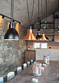 Long dining table, pendant lights above it in the dining room with rustic exposed brickwork