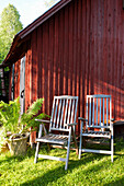 Two wooden chairs in front of a red-brown wooden house