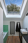 Bathtub with green tiles in modern bathroom with skylight