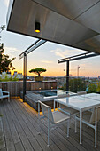 Wooden roof terrace with table, chairs and pool at sunset
