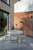 Runder Tisch mit Stühlen auf Terrasse mit Terrazzoboden vor Ziegelmauer