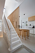 Staircase with white steps and wooden slats as partition to open-plan kitchen with island counter