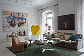 Sofa with a fur blanket and cushions, coffee table and armchair, in the background ear sculpture and painting above a console tab;e