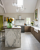 Vintage glass globes define space above marble kitchen island with sunflowers